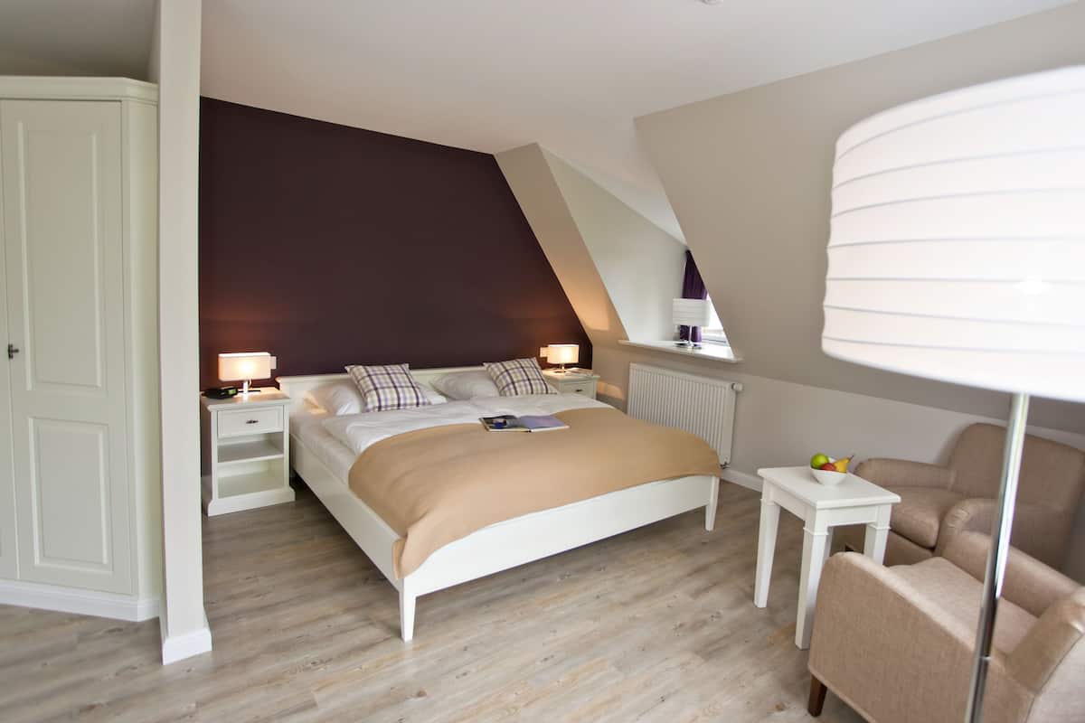 Un dormitorio con una cama, mesitas de noche, una silla, una lámpara y una ventana.