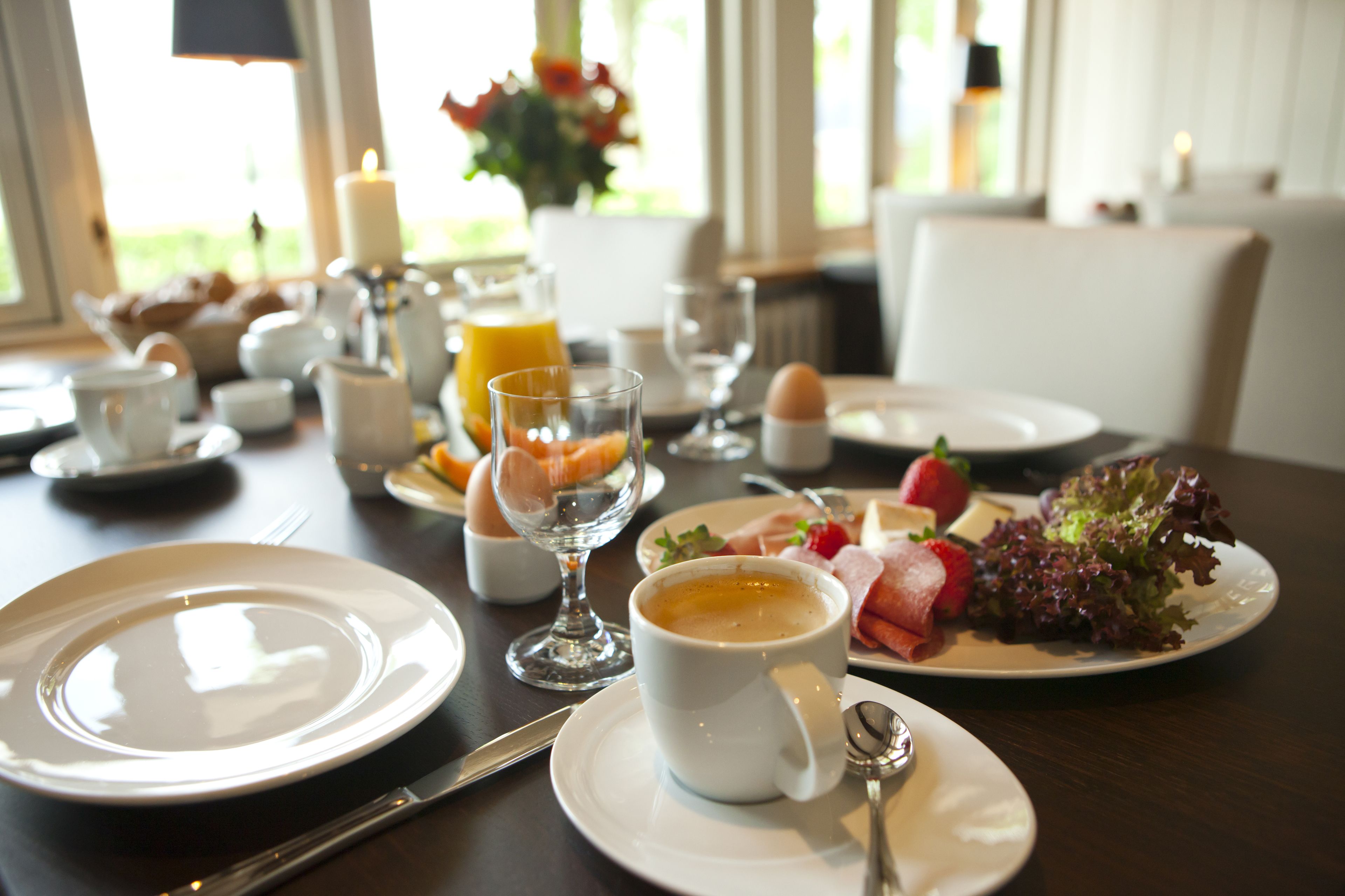 Una escena de desayuno con platos, tazas y diversos alimentos sobre una mesa.