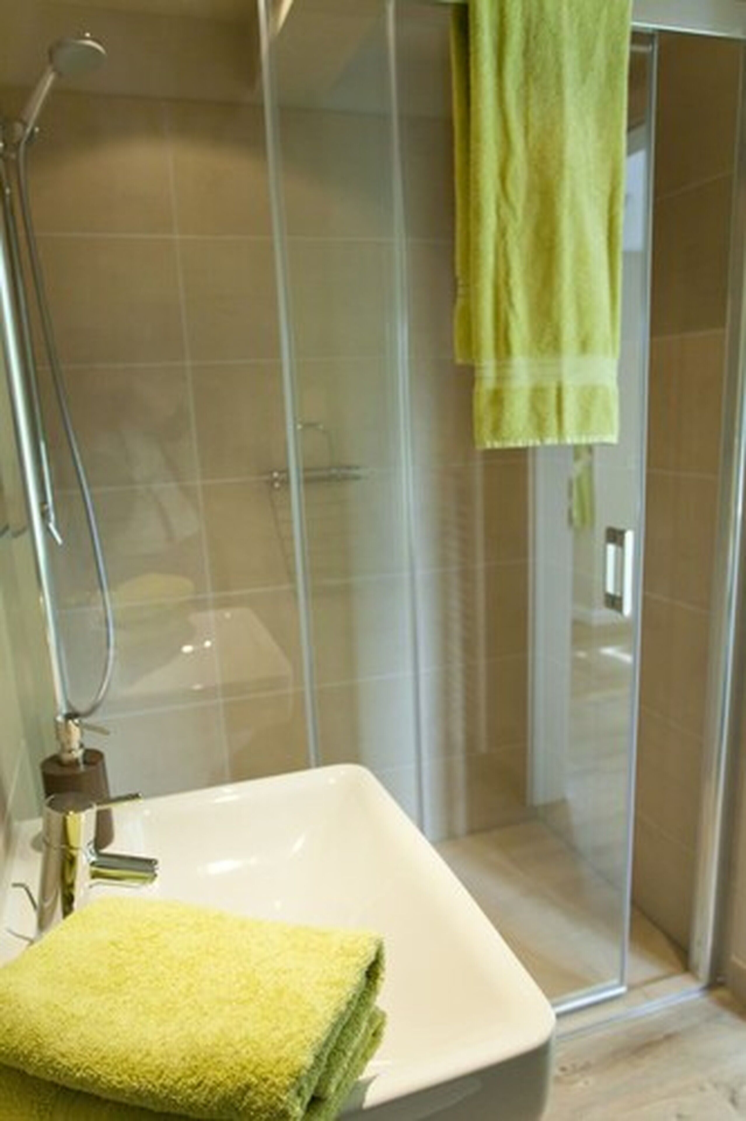 Un baño con ducha de mampara de vidrio, un lavamanos blanco y una toalla amarilla.