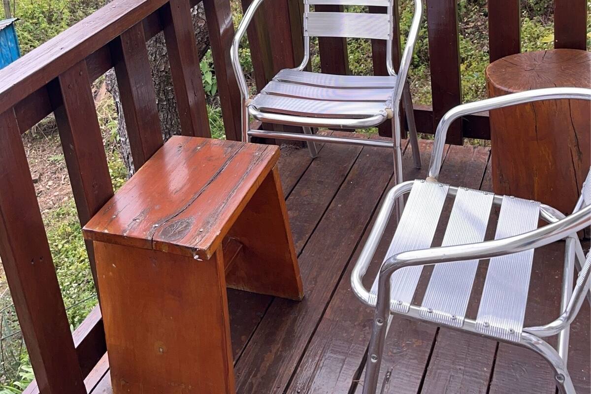 A wooden deck with two metal chairs and a small table, surrounded by trees and a wooden railing.