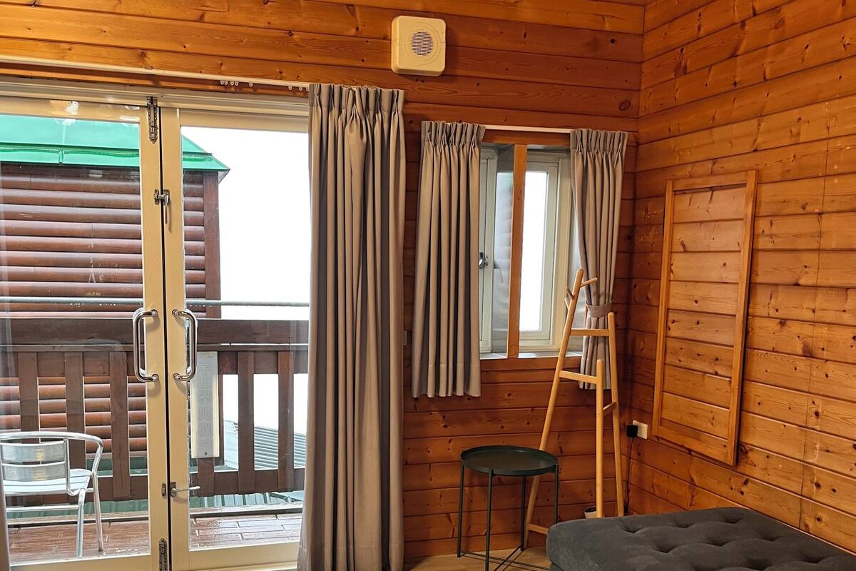 A wooden cabin interior with a sliding glass door, a small table, a sofa, and a ladder leaning against the wall.