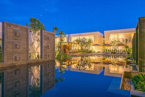 Un hotel moderno con una piscina reflectante, asientos al aire libre y un cielo nocturno despejado.