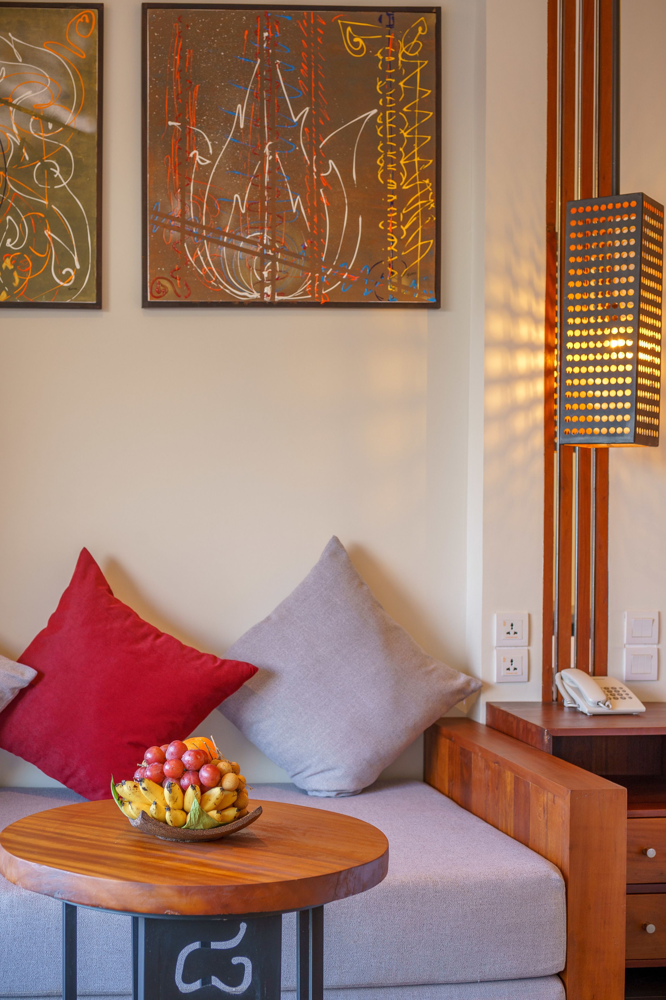 Een moderne woonkamer met een bank, een ronde houten tafel met een schaal fruit, en twee abstracte schilderijen aan de muur.