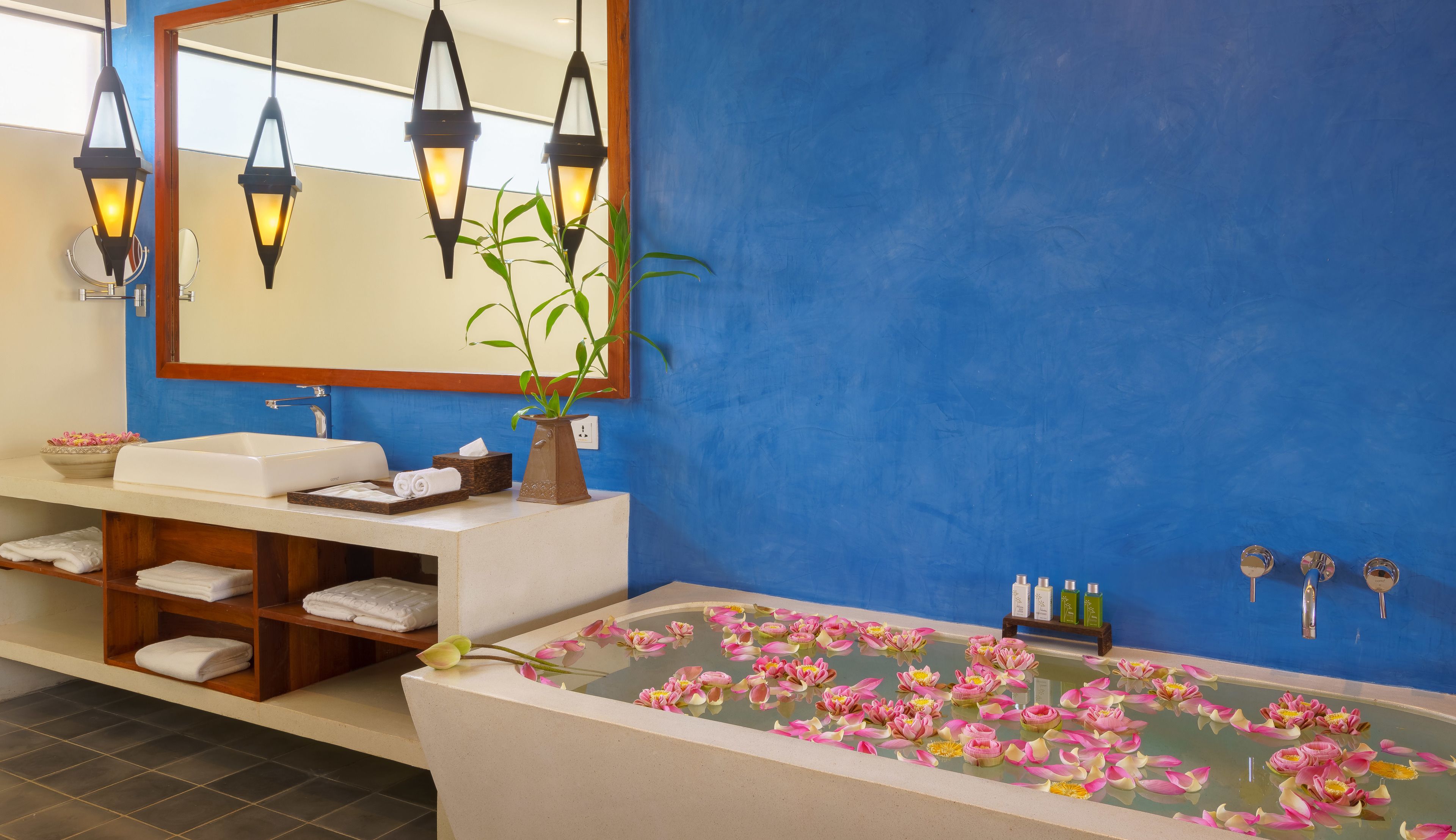 Un baño con una bañera llena de flores rosadas, un espejo, un lavamanos y un estante con toallas.