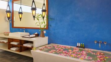 Un baño con una bañera llena de flores rosadas, un espejo, un lavamanos y un estante con toallas.