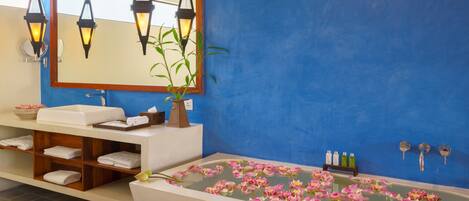 Un baño con una bañera llena de flores rosadas, un espejo, un lavamanos y un estante con toallas.
