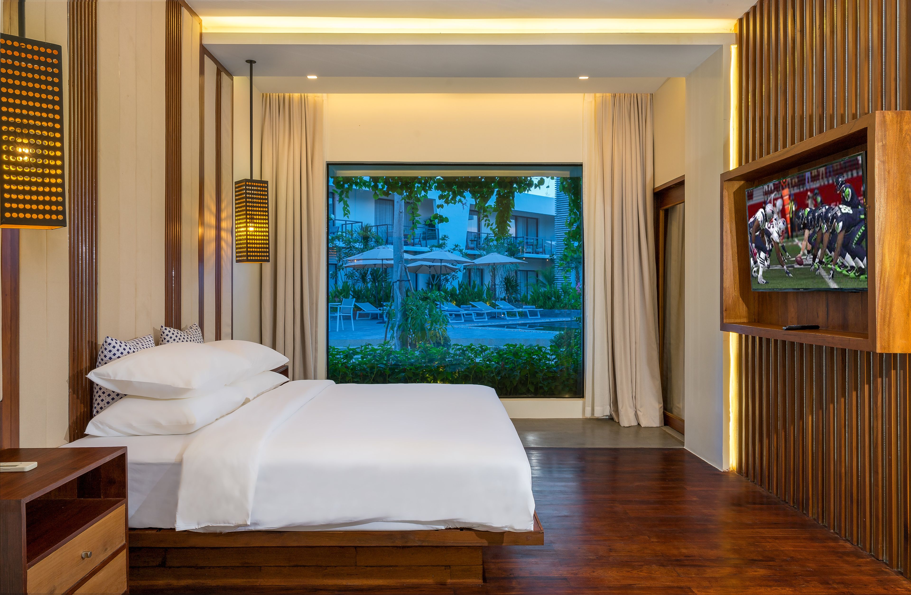 Une chambre d’hôtel avec un grand lit, un téléviseur fixé au mur et une vue sur l’espace extérieur abritant une piscine.