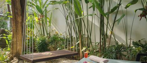 A tranquil outdoor relaxation area with a swing, a massage table, and lush greenery.