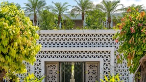 A white lattice gate with a central door, surrounded by lush greenery and palm trees. - Metta Residence & Spa (Siem Reap)
