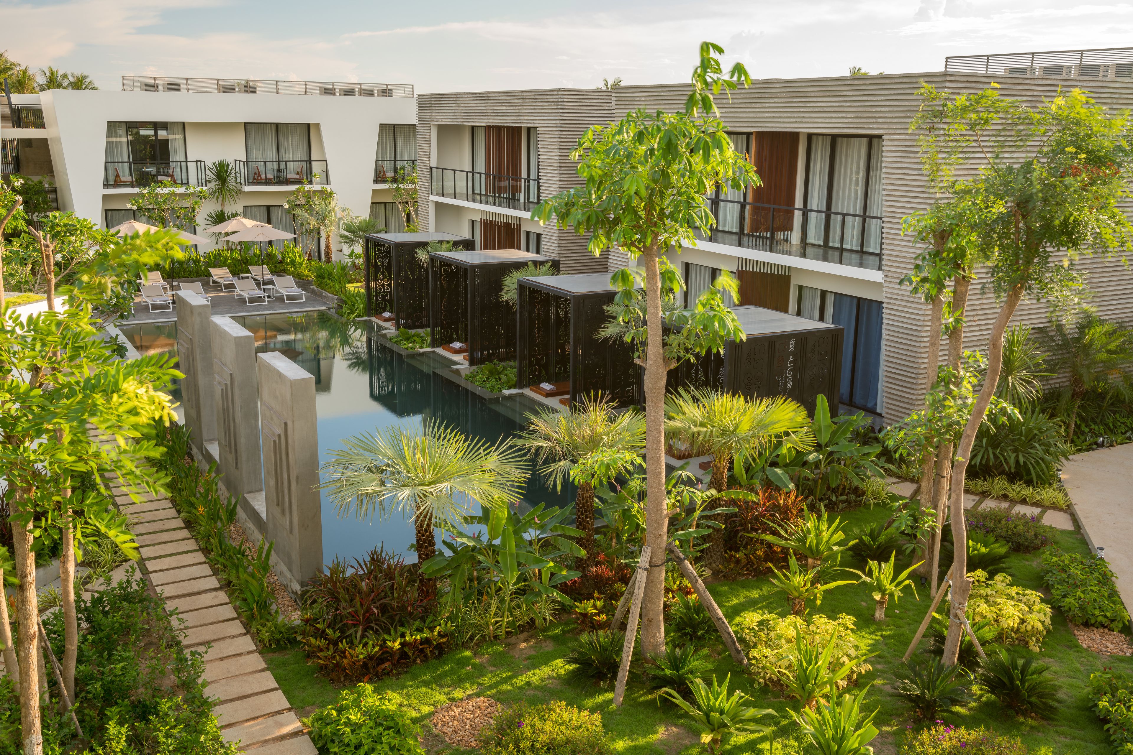 A modern hotel with a swimming pool surrounded by lush greenery and palm trees.