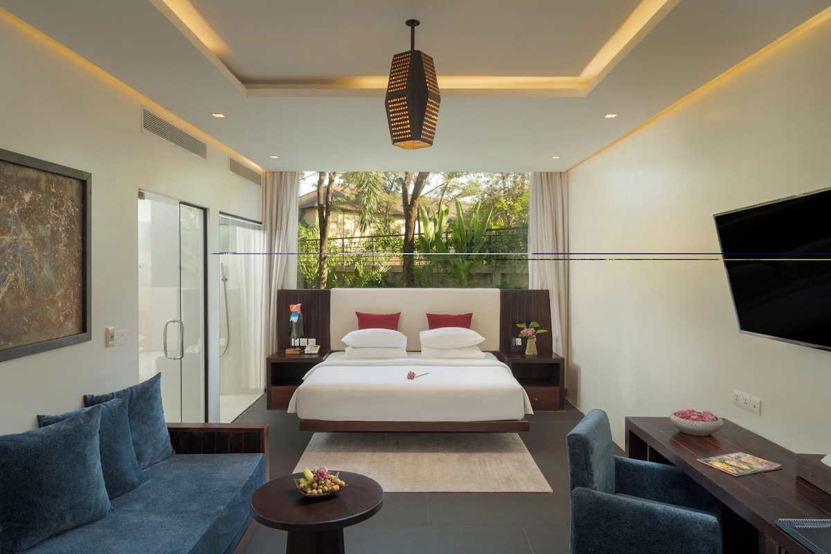 A modern hotel room with a large bed, a TV, a desk with a chair, and a sofa.