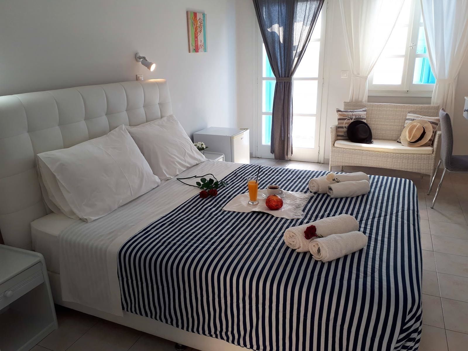A neatly made bed with a striped bedspread, a bedside lamp, and a small table with a glass of orange juice, a cup of coffee, and a red apple.