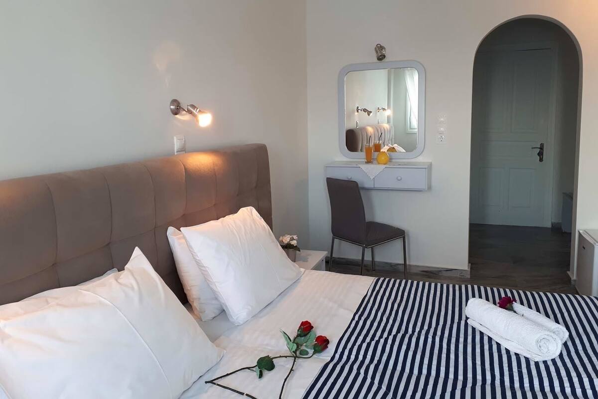 A hotel room with a bed, a bedside table, a chair, a mirror, and a door.