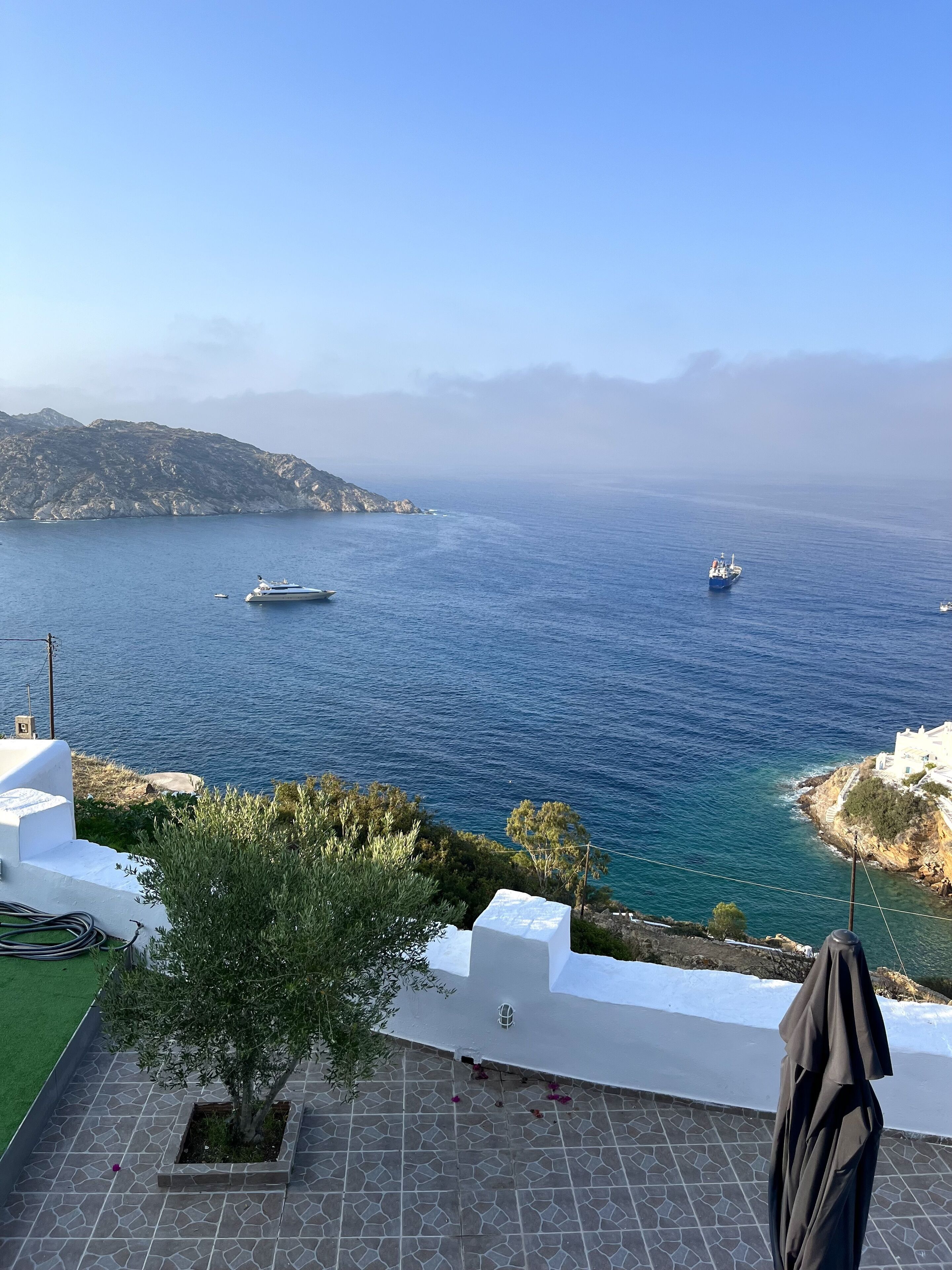 Une vue sur la côte, avec une terrasse, un bâtiment blanc et des bateaux sur la mer.