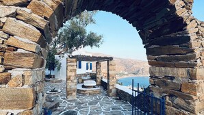A stone archway leading to a building with a stone-paved courtyard and a view of the sea. - Petradi Hotel (Ios)