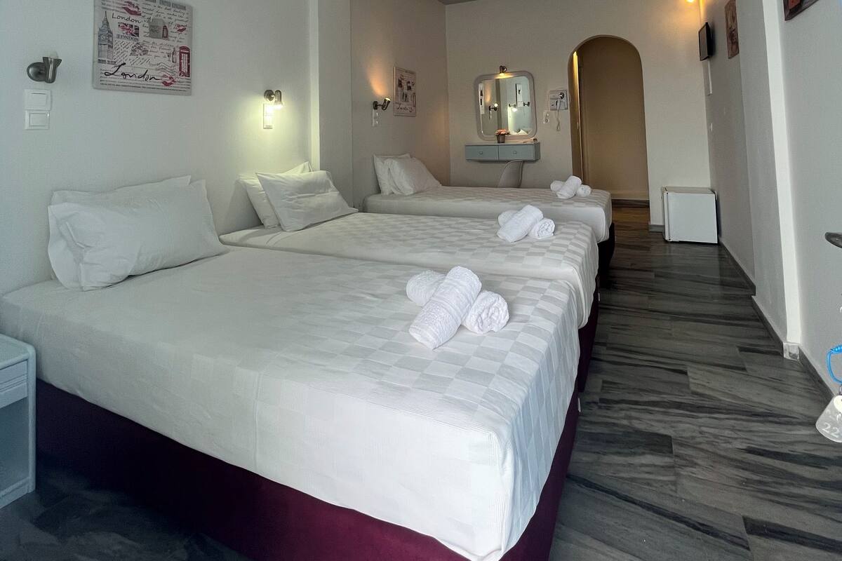 A hotel room with two beds, a marble floor, a mirror, and a picture of London on the wall.
