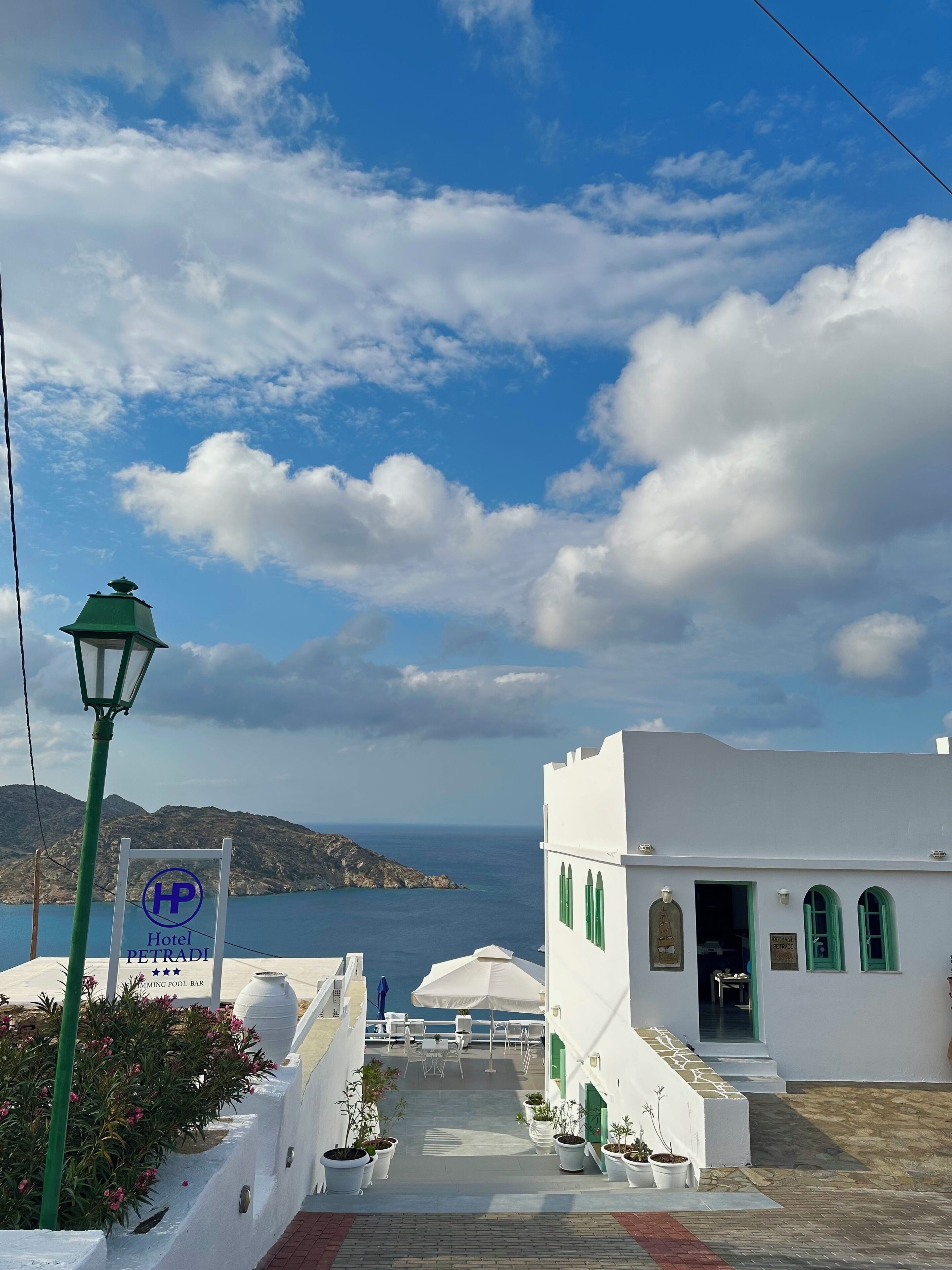 A white building with green accents, a sign for 'Hotel PELTRADI', and a view of the sea.