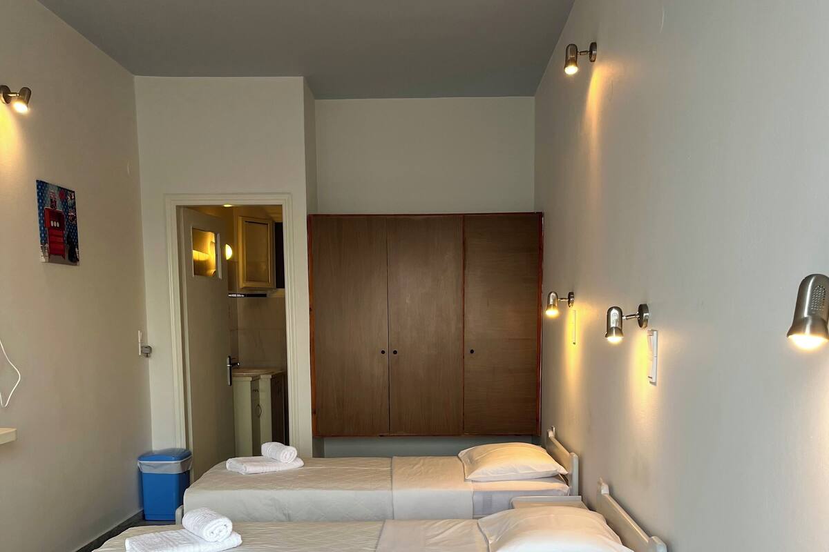 A hotel room with three beds, a wardrobe, and wall-mounted lights.