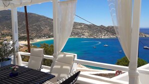 A terrace with a table and chairs overlooking a coastal view with boats and a beach. - Petradi Hotel (Ios)