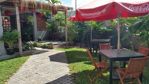 Un patio con mesa y sillas, rodeado de plantas en macetas y una estructura de techo de paja.