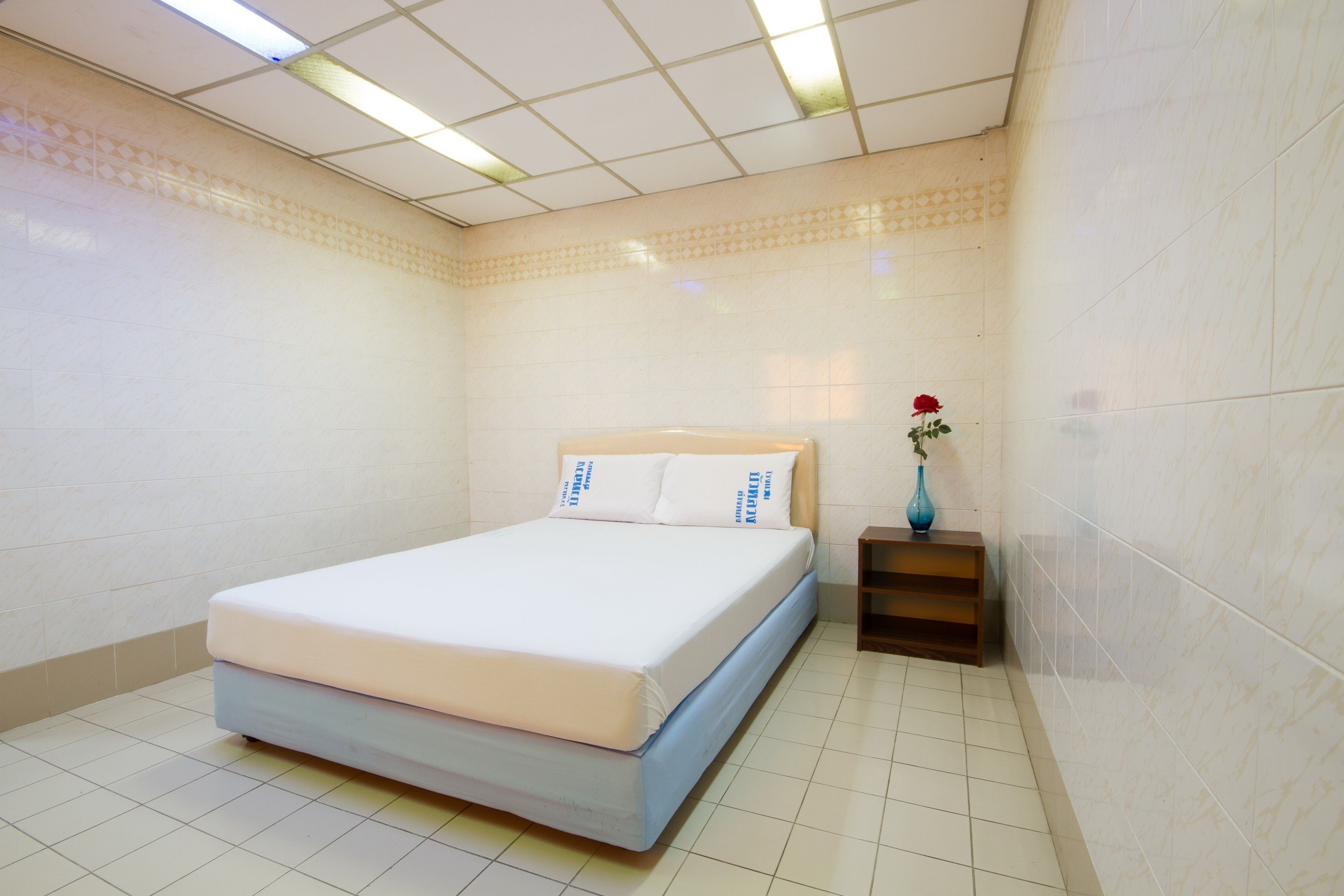 Un dormitorio ordenado con una cama, una mesita de noche y un florero con una flor.