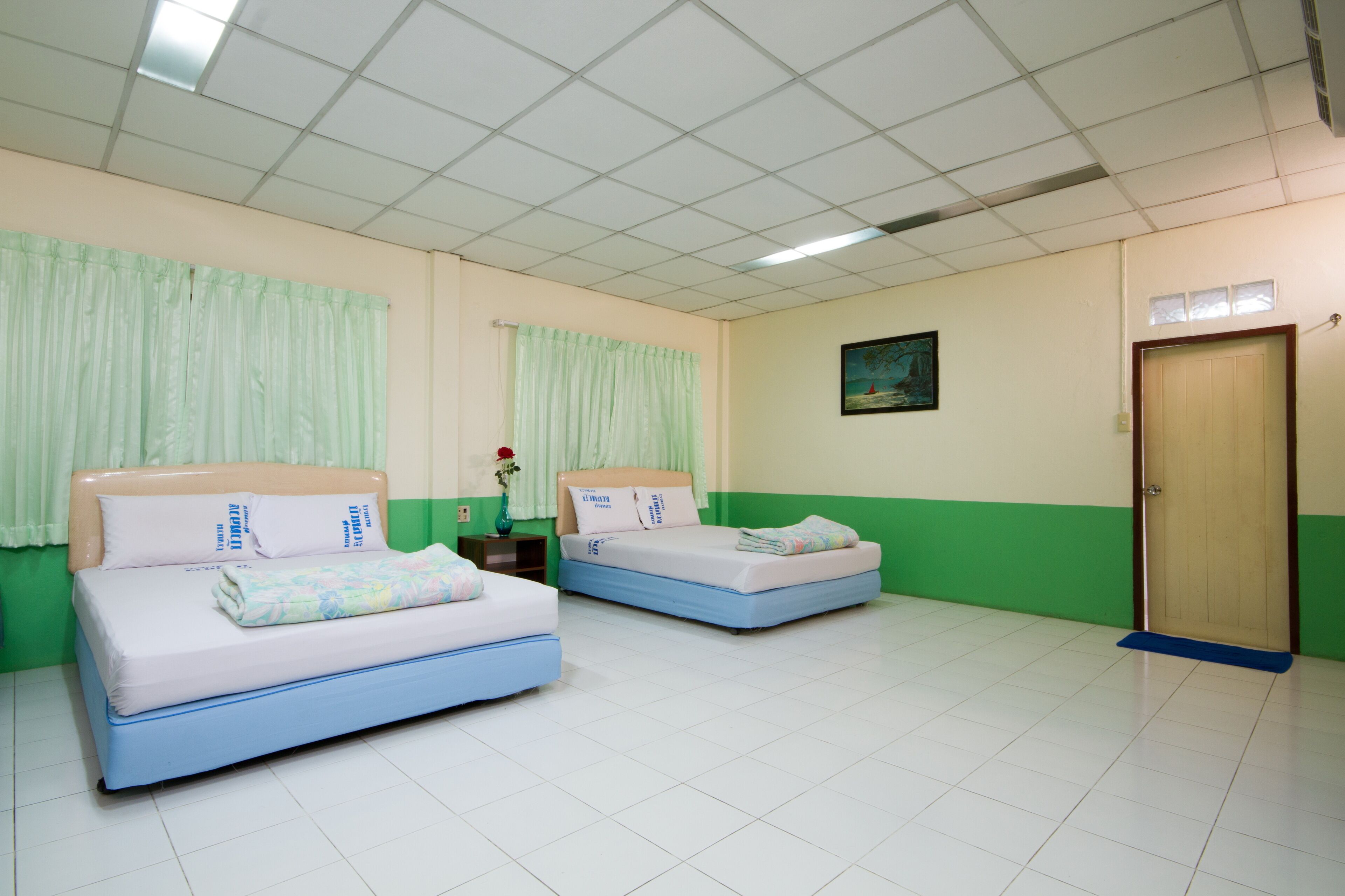 A room with two beds, a wooden door, a painting on the wall, and a tiled floor.