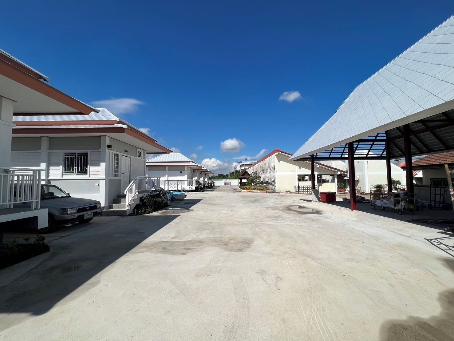 A row of white buildings with red roofs, a paved driveway, and a clear blue sky.