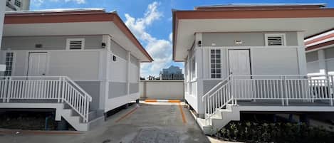 Une rangée de bâtiments à deux étages, avec une allée centrale, chaque bâtiment étant doté d’une porte et d’un petit balcon.