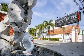 Entrada de un hotel con un letrero grande, una estatua de cisne y palmeras al fondo.