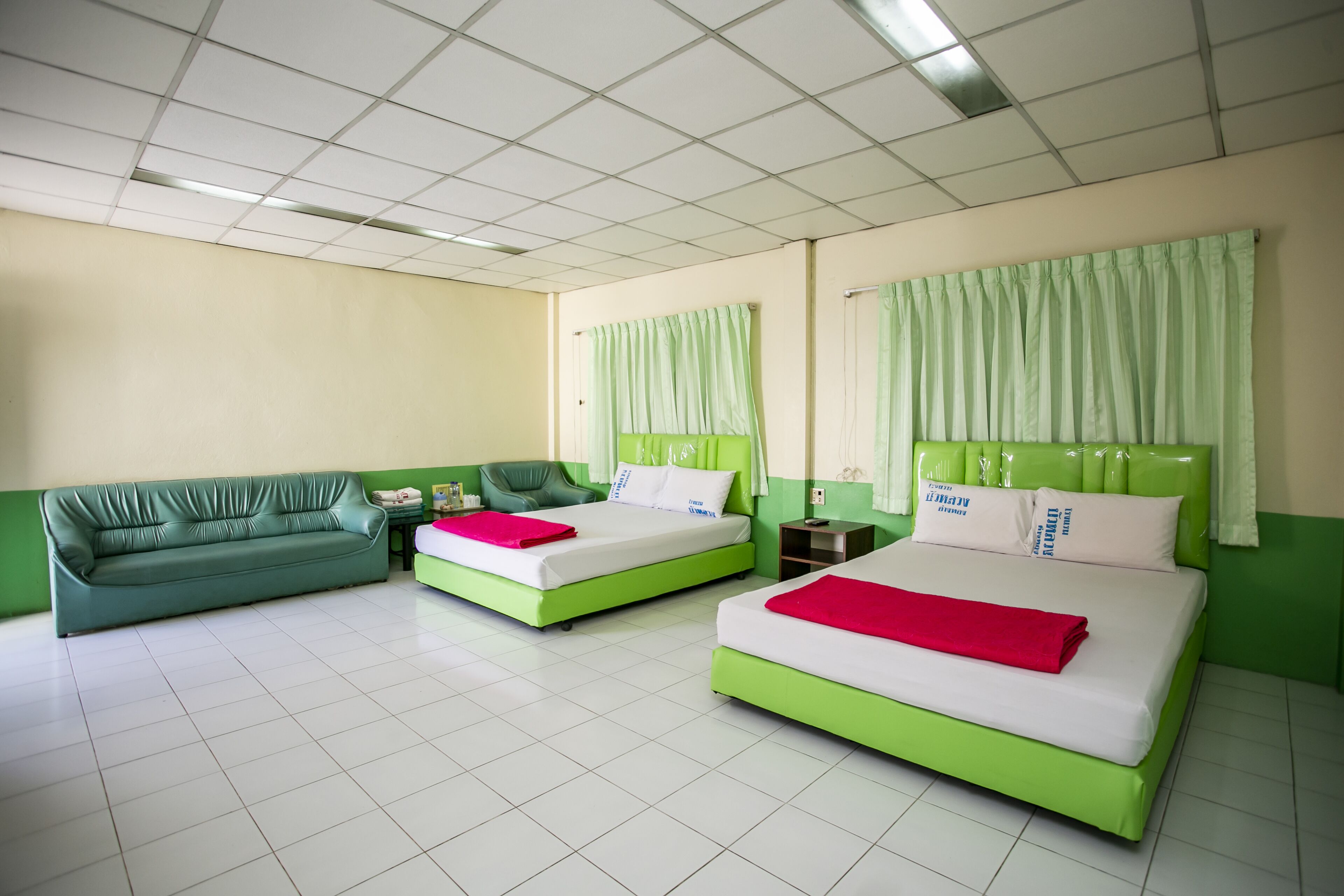 A hotel room with two beds, a green sofa, and a small table.