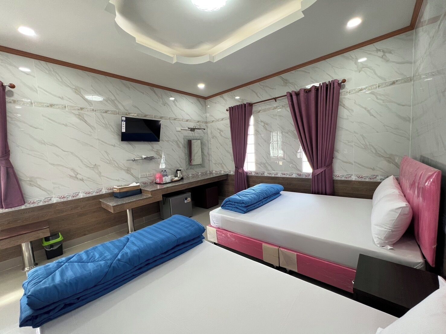 Una habitación de hotel con cama, escritorio, televisor y ventana con cortinas.