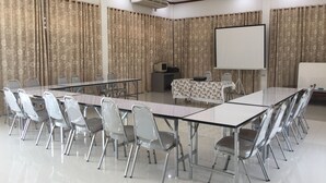 Un salón de conferencias con una larga mesa, sillas, una pantalla de proyector y cortinas.