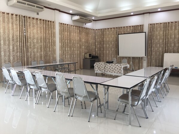 Un salón de conferencias con una larga mesa, sillas, una pantalla de proyector y cortinas.