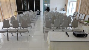 Un salón de conferencias con filas de sillas y mesas, un proyector y una máquina de café.