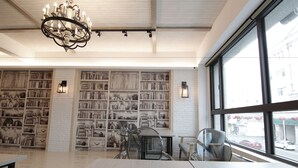 A spacious room with a large window, a chandelier, and bookshelves filled with books and decorative items.