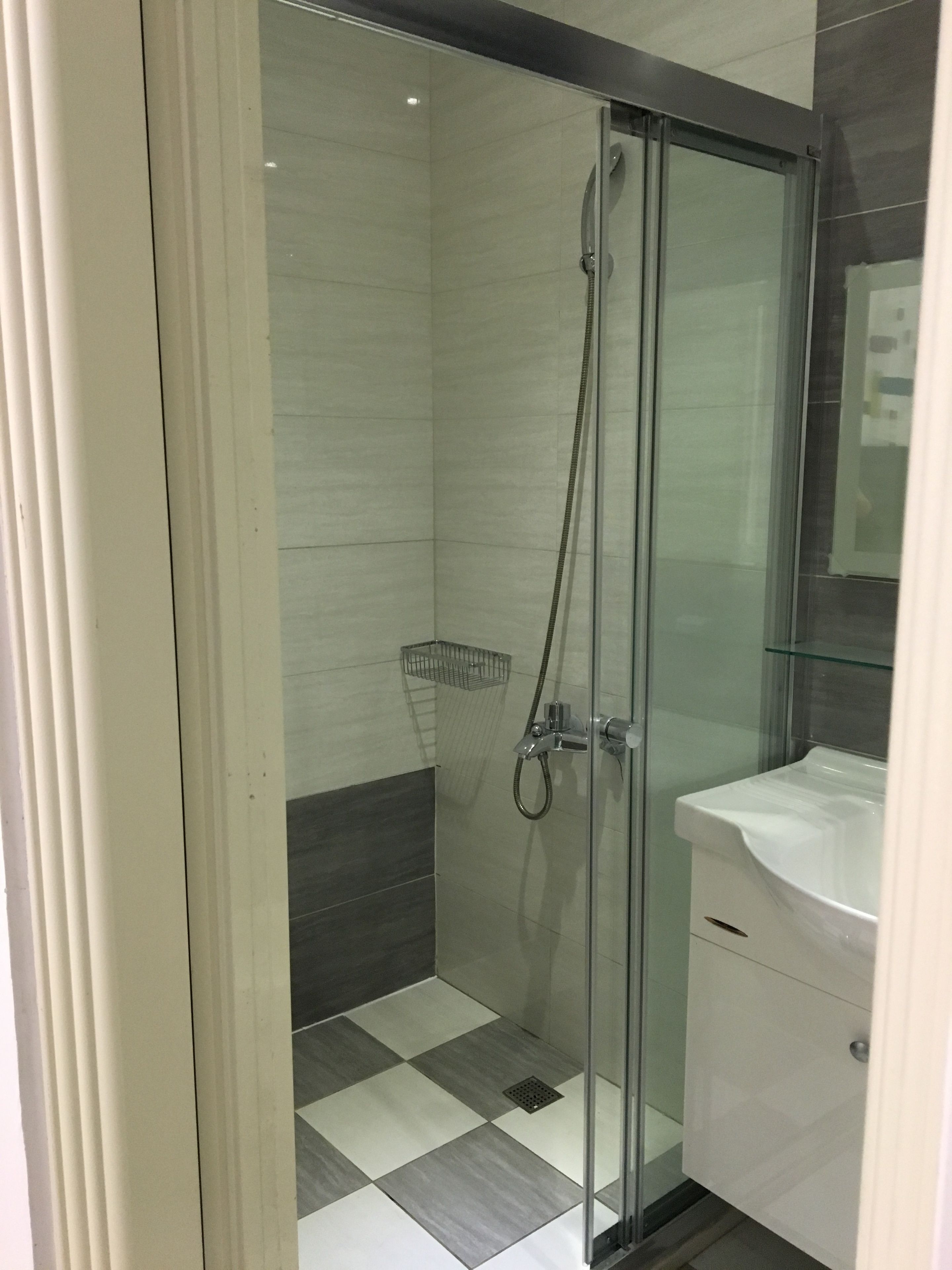 A modern bathroom with a glass-enclosed shower, a white sink, and checkered floor tiles.