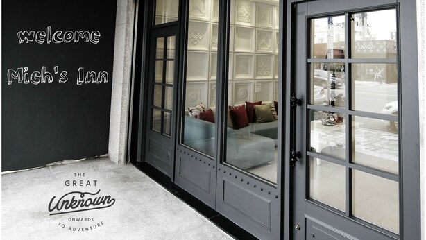 A modern hotel entrance with a large glass door, a welcoming sign, and a view of the street outside.
