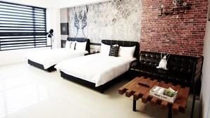 A modern hotel room with two beds, a black leather sofa, a wooden coffee table, and a brick wall with a clock.