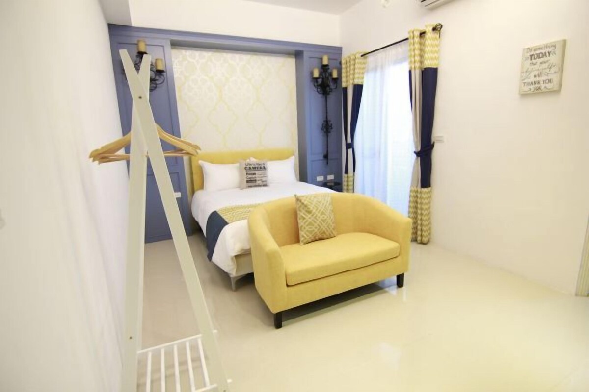A bedroom with a bed, a yellow sofa, a wardrobe, and a hanging light fixture.