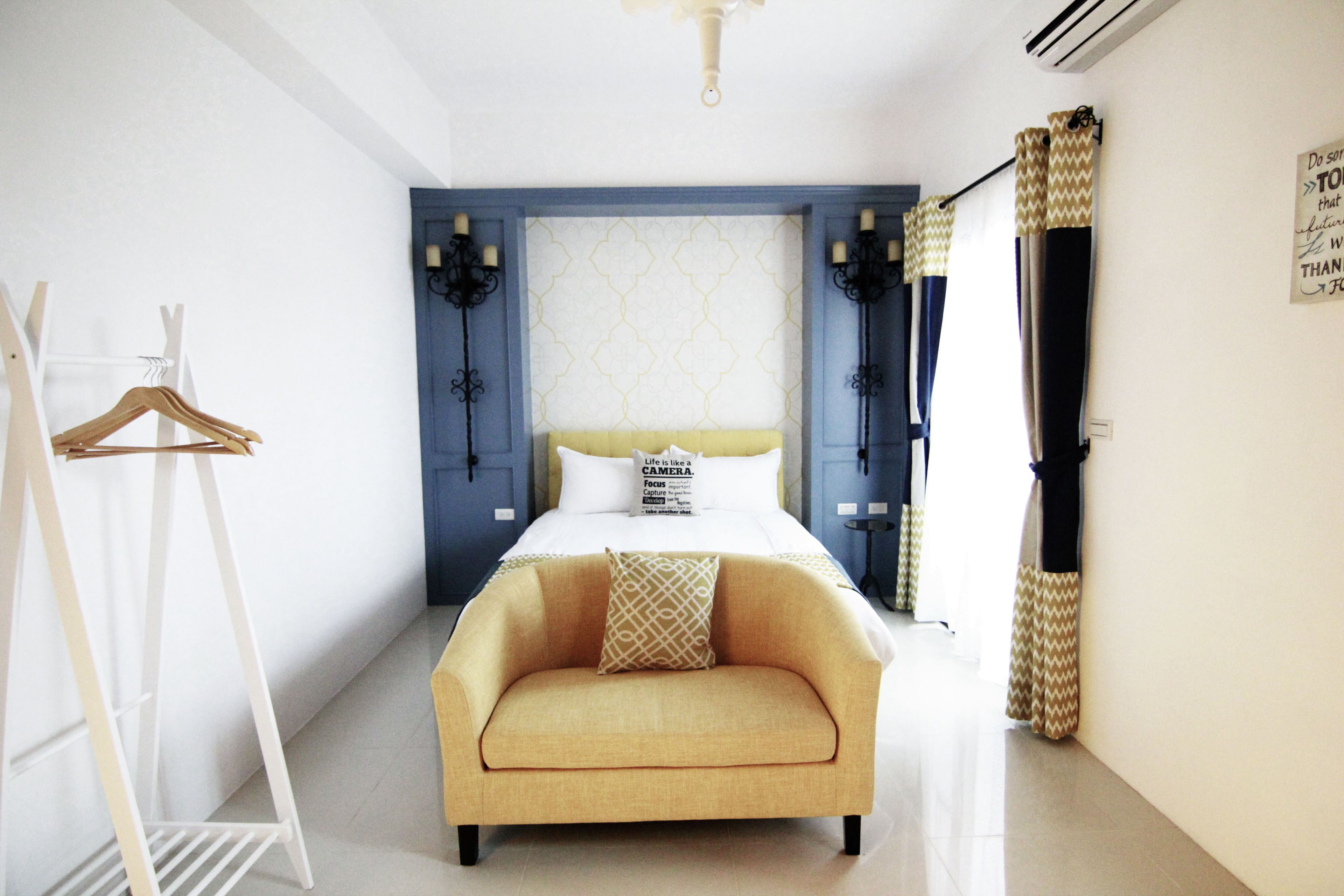 A bedroom with a bed, a sofa, a coat rack, and a wall with a decorative pattern.
