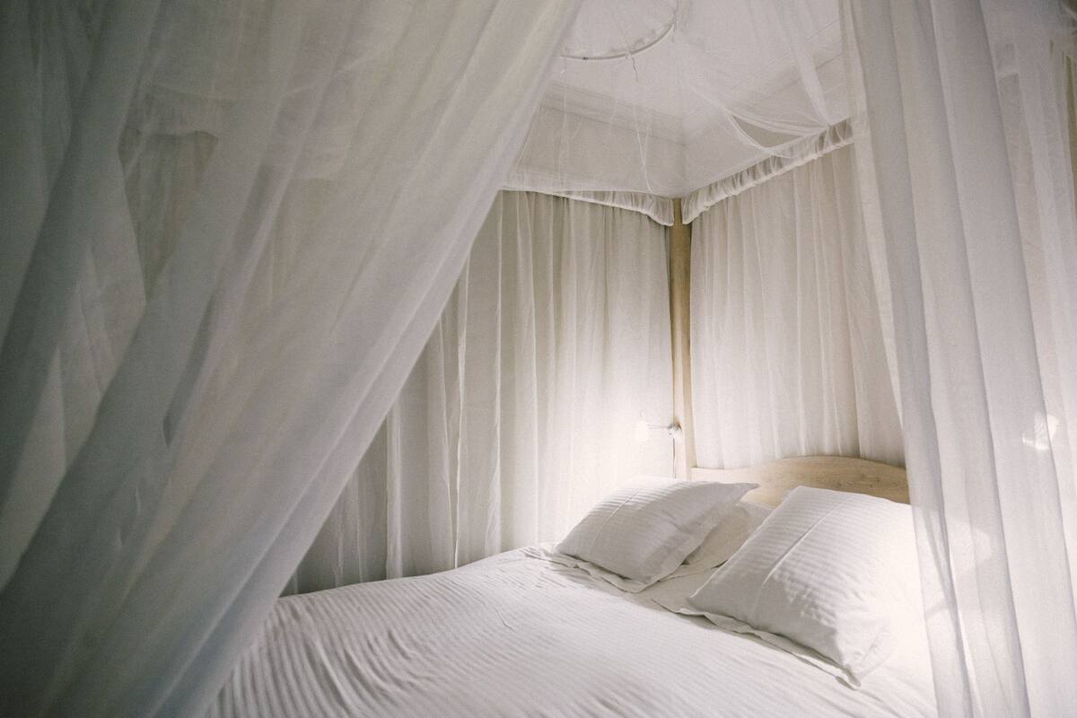 A bedroom with a canopy bed, white bedding, and a wooden headboard.