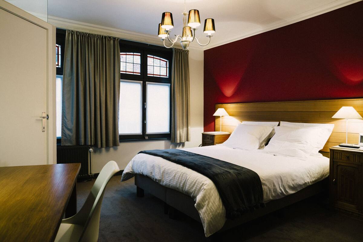 A hotel room with a bed, bedside tables, a desk, and a chair.