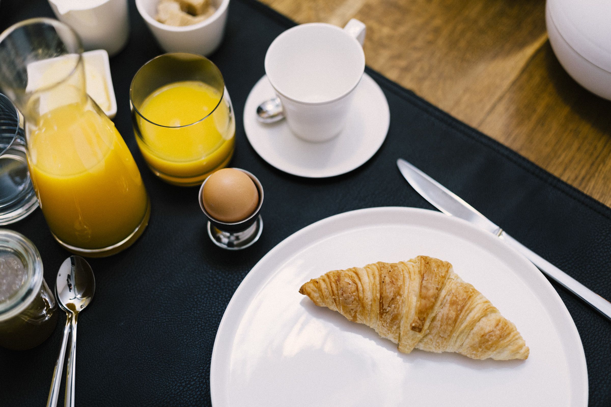 Une table mise pour le petit-déjeuner avec un croissant sur une assiette, un verre de jus d'orange, une tasse de café et un petit bol de sucre.