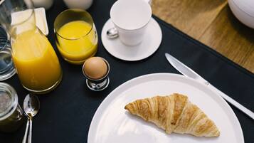 A breakfast setting with a croissant on a plate, a glass of orange juice, a cup of coffee, and a small bowl of sugar.