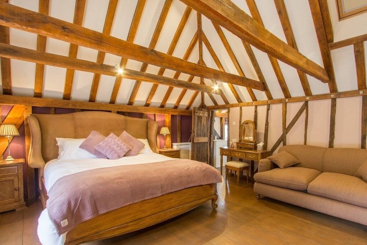 Un dormitorio con techo de madera, una cama grande con cabecera, un sofá y un aparador.
