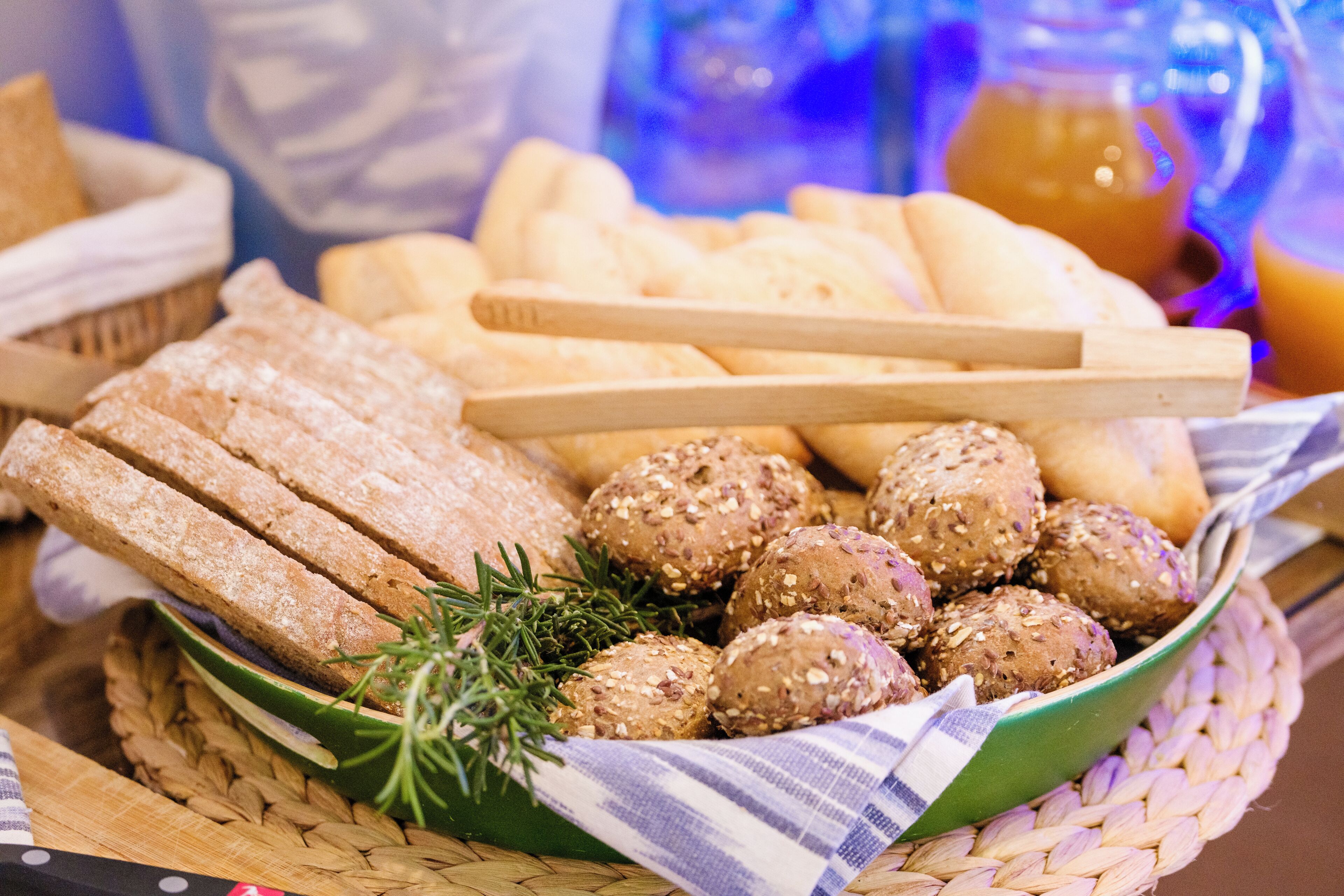 Un panier rempli d’un assortiment de pains et de petits pains, notamment des variétés à grains entiers et aux graines, posé sur un tapis tressé.