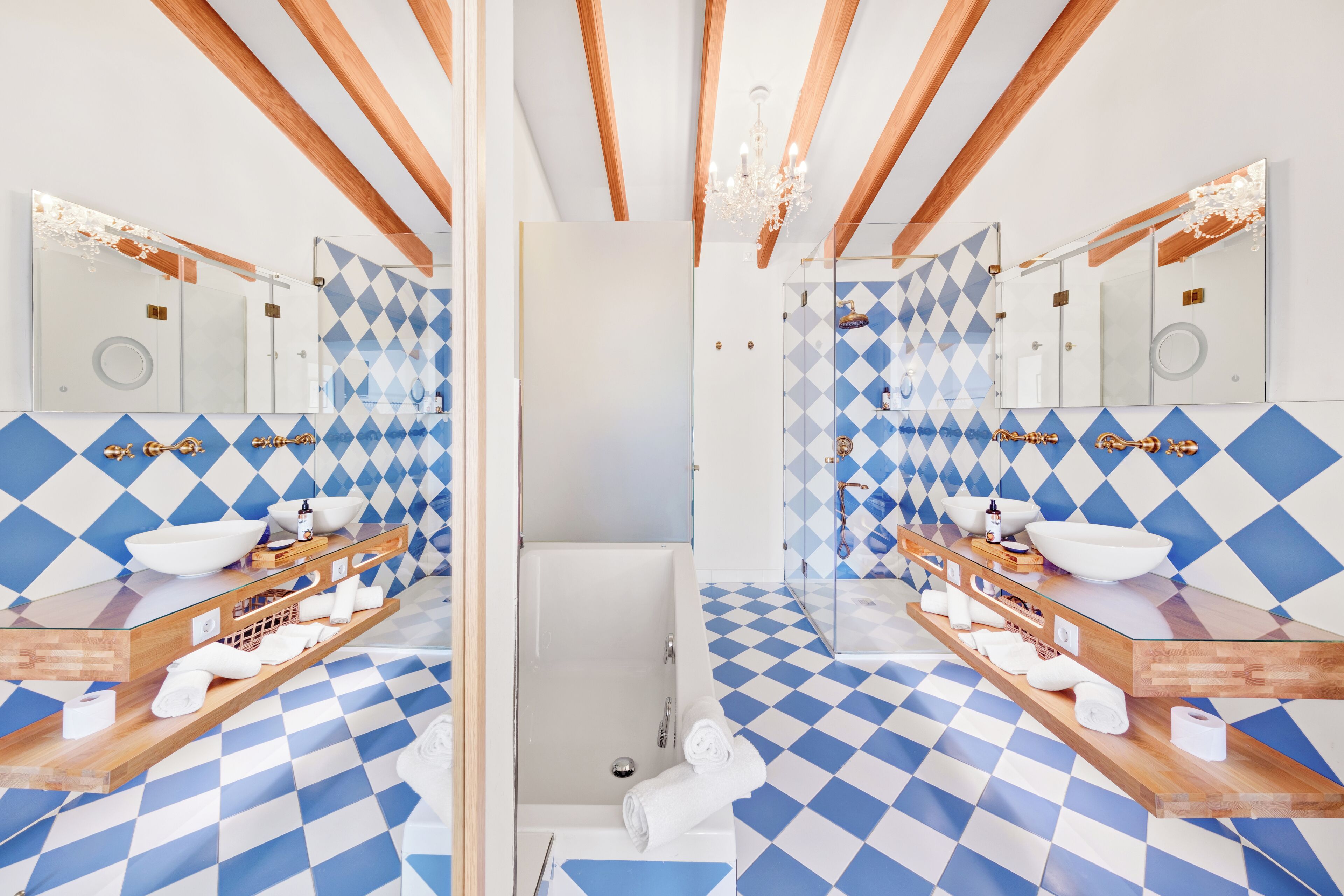 A mirrored bathroom with checkered blue and white tiles, wooden beams, and a glass vanity with a white sink and towel rack.