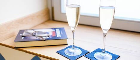 Zwei Sektgläser auf blauen Servietten auf einem Holztisch, neben ihnen ein Buch und Gläser.