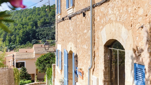 A narrow stone pathway flanked by buildings with blue shutters, leading to an arched doorway. - Es Corte Vell - Inland Bunyola - Adults Only (Bunyola)