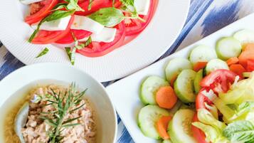 Ein Tisch mit drei Tellern Essen: ein Tomaten-Mozzarella-Salat, ein Gurken-Karotten-Salat und eine Schüssel Thunfischsalat mit Kräutern.